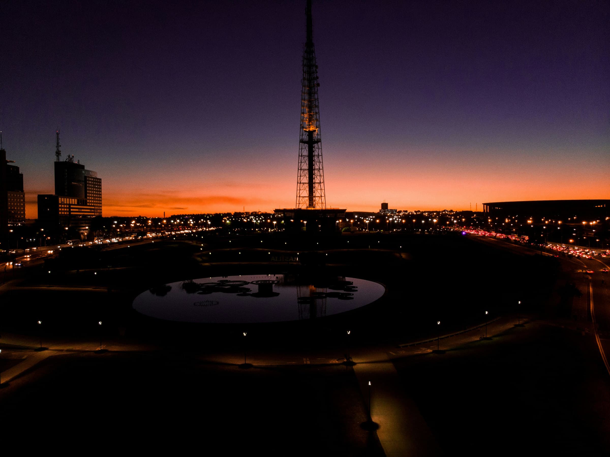 Brasília ao anoitecer, com a Torre de TV em contraluz sobre o céu alaranjado e as luzes da cidade no Eixo Monumental